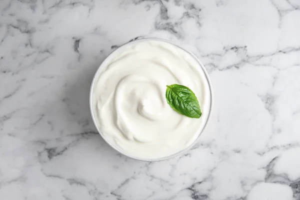 Bowl of fresh sour cream with basil on white marble table, top view — Stock Photo, Image