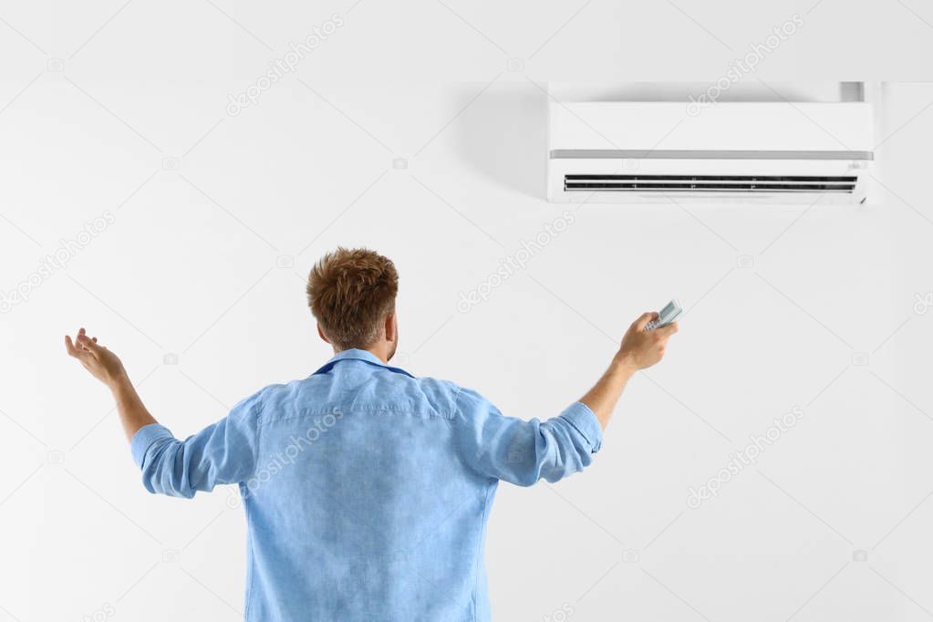 Young man operating air conditioner with remote control indoors