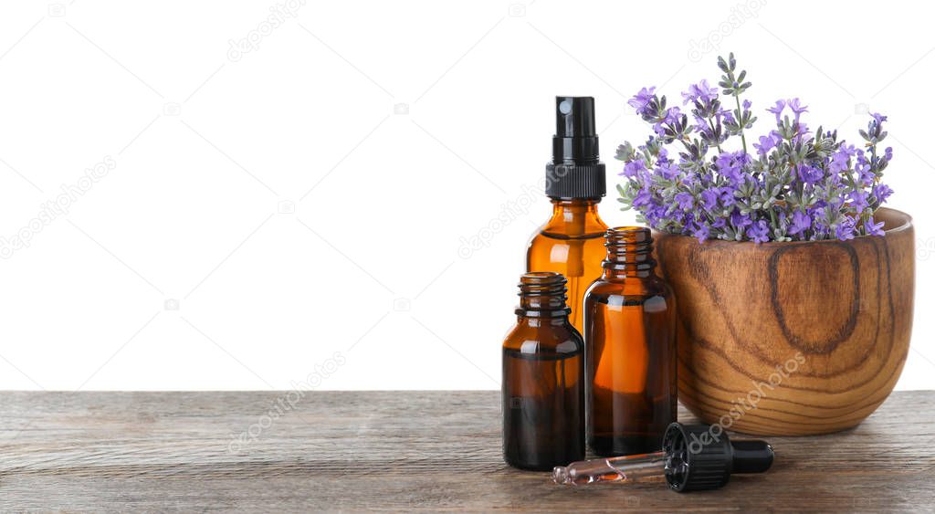 Bottles of essential oil and bowl with lavender flowers on wooden table against white background