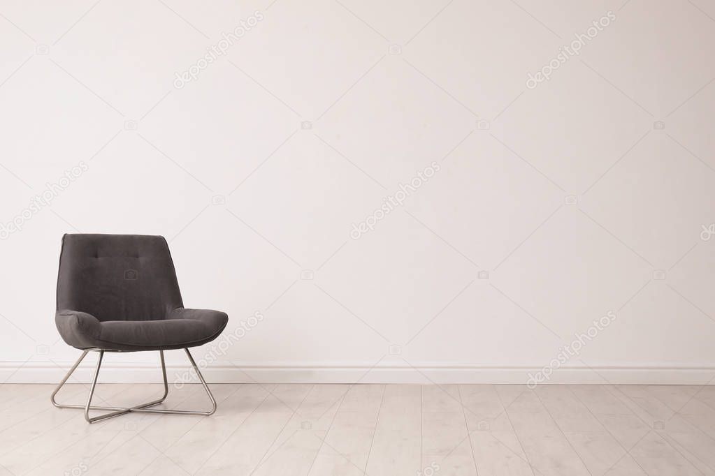Stylish comfortable chair near white wall, space for text. Interior design