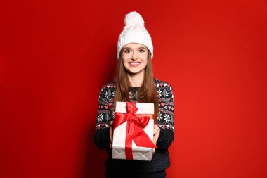 Kırmızı arka plan üzerinde hediye kutusu tutan Noel kazak genç kadın