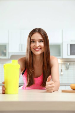 Young woman with bottle of protein shake in kitchen clipart
