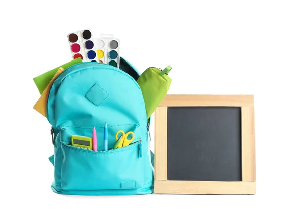 Рюкзак, повний різних шкільних канцелярських товарів і маленької порожньої дошки на білому тлі. Простір для тексту — стокове фото