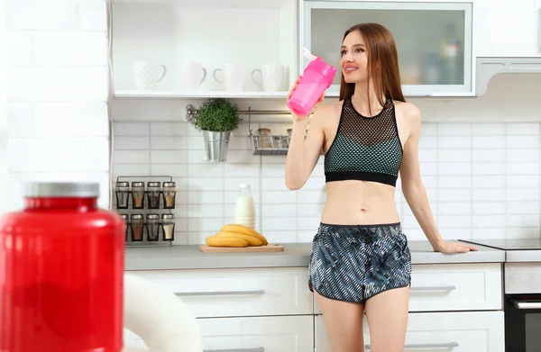 Giovane donna che beve frullato proteico in cucina — Foto Stock