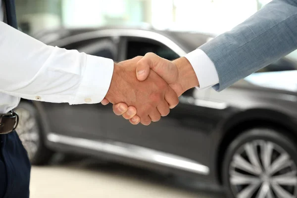 現代の自動車販売店でクライアントと握手する若いセールスマン、クローズアップ — ストック写真