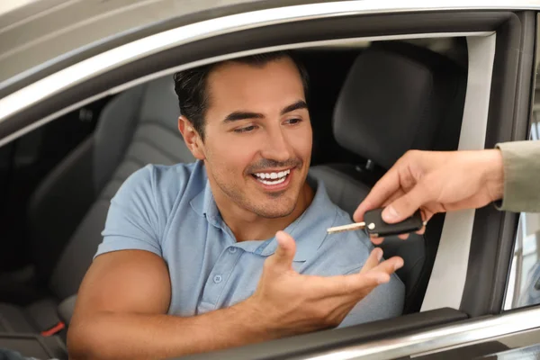 Jovem vendedor dando chave de carro para o cliente na concessionária automóvel moderna, close-up — Fotografia de Stock