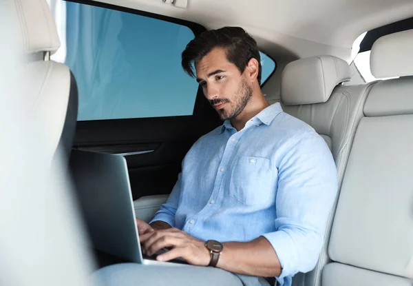 Ελκυστικός νέος άνθρωπος που εργάζεται με φορητό υπολογιστή στο πίσω κάθισμα στο πολυτελές αυτοκίνητο — Φωτογραφία Αρχείου