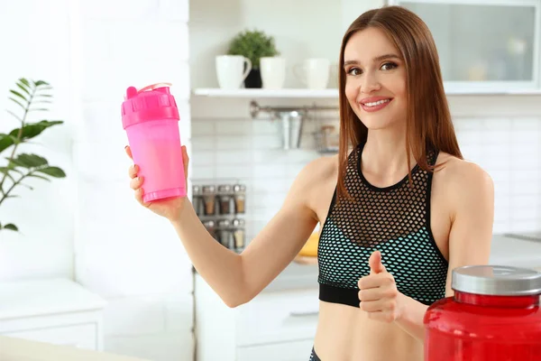 Jovem com garrafa de batido de proteína na cozinha — Fotografia de Stock