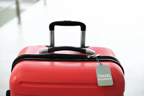 Stylish suitcase with travel insurance label on blurred background, closeup. Space for text — Stock Photo, Image