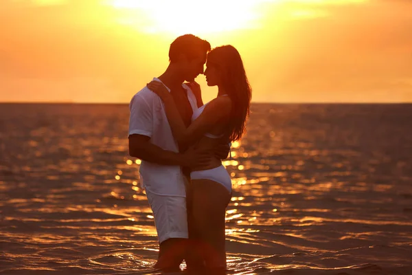 Onnellinen nuori pari viettää aikaa yhdessä meren rannalla auringonlaskun aikaan — kuvapankkivalokuva