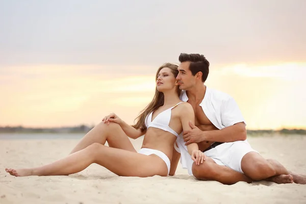 Feliz pareja joven relajándose juntos en la playa al atardecer —  Fotos de Stock