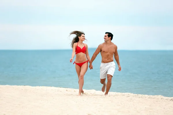 Feliz jovem casal correndo juntos na praia do mar — Fotografia de Stock