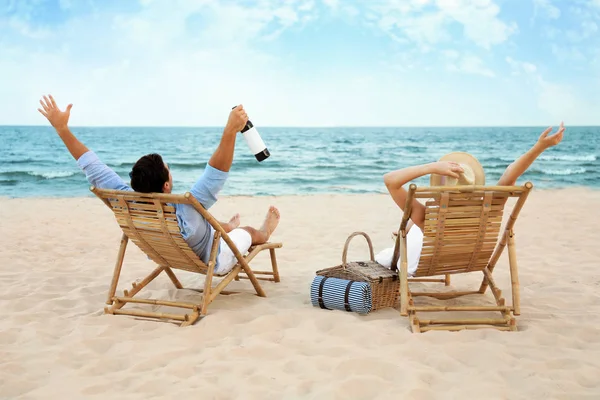 Feliz pareja joven con vino sentado en tumbonas en la playa de mar Imágenes De Stock Sin Royalties Gratis