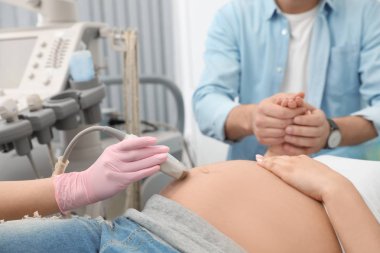 Klinikte ultrason taraması sırasında eşini destekleyen adam, yakın çekim görünümü