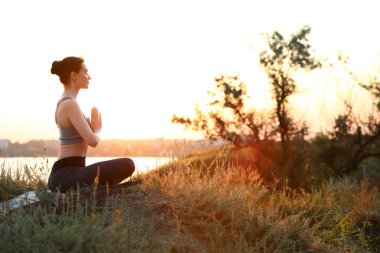 Genç kadın gün batımında açık havada yoga yapıyor. Zen meditasyonu