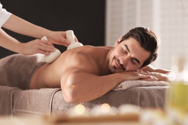 Spa salonunda bitkisel torba masajı alan yakışıklı genç adam