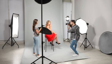 Asistan modern stüdyoda genç kadının fotoğrafını çeken profesyonel fotoğrafçı