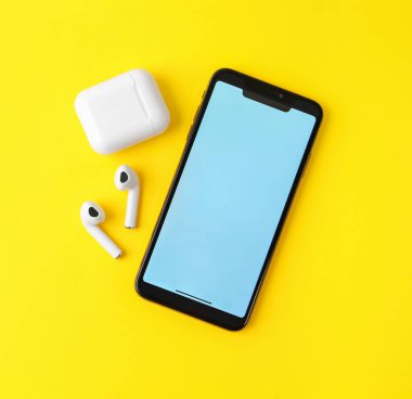 Kablosuz kulaklıklar, cep telefonu ve şarj kılıfı sarı arka plan, düz yatıyordu. Metin için alan