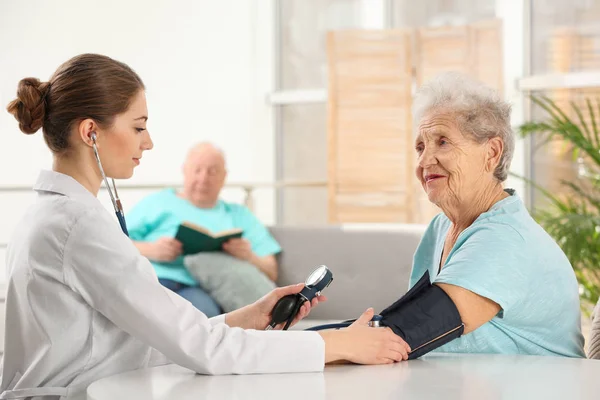 Enfermera midiendo la presión arterial de una anciana en el interior. Ayudar a las generaciones mayores —  Fotos de Stock