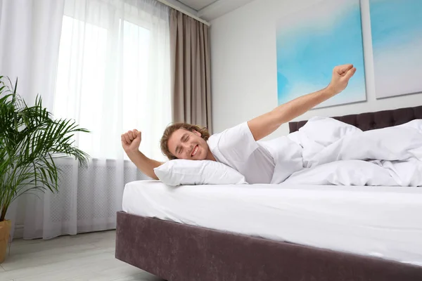 Sleepy young man stretching while lying under blanket in morning. Bedtime — Stock Photo, Image