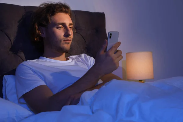 Красивый молодой человек, использующий смартфон в темной комнате ночью. Время спать — стоковое фото