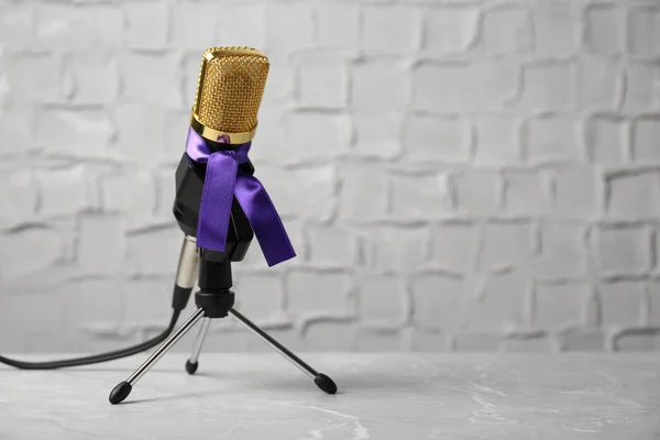 Microphone avec ruban de sensibilisation violet sur la table contre le mur blanc, espace pour le texte — Photo