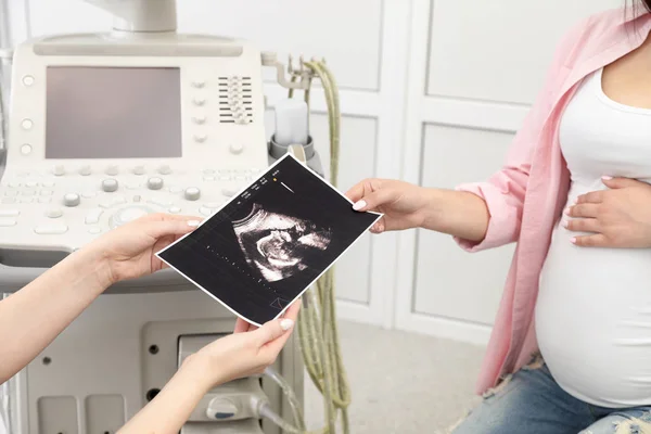 Doctor showing ultrasound image of baby to future mother in clinic, closeup — Stock Photo, Image