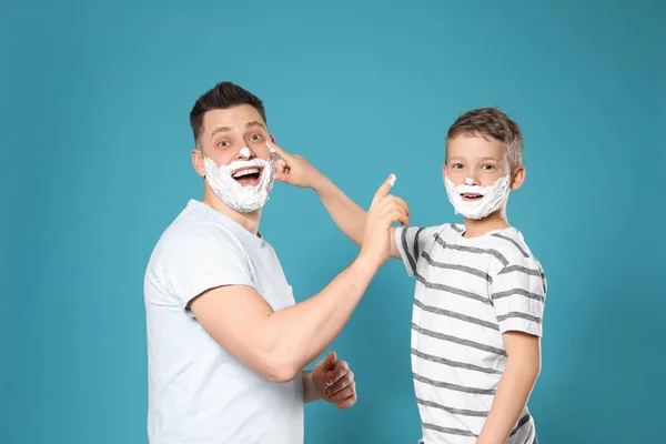 Joyeux papa et fils avec mousse à raser sur les visages sur fond bleu — Photo