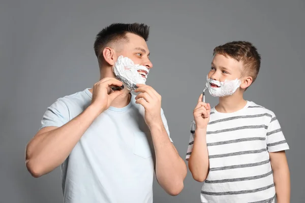 Tata golenie i syn naśladując go na szarym tle — Zdjęcie stockowe