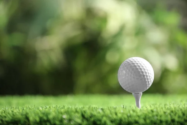Bola de golfe com tee na grama artificial contra fundo desfocado, espaço para texto — Fotografia de Stock