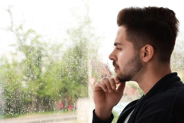 Pensativo hombre guapo cerca de la ventana en el interior en el día lluvioso — Foto de Stock