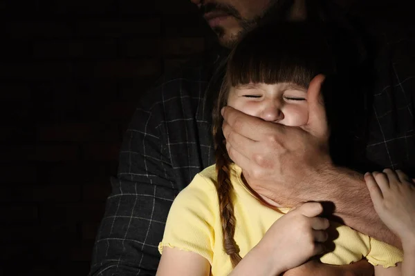 Homem adulto cobrindo a boca da menina assustada no fundo escuro, espaço para texto. Criança em perigo — Fotografia de Stock