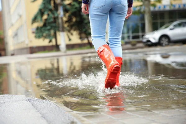 水たまりの中に赤いゴムのブーツを持つ女性、クローズアップ。雨天 — ストック写真