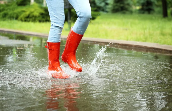 赤いゴムのブーツを持つ女性が水たまりに飛び込み、クローズアップ。雨天 — ストック写真