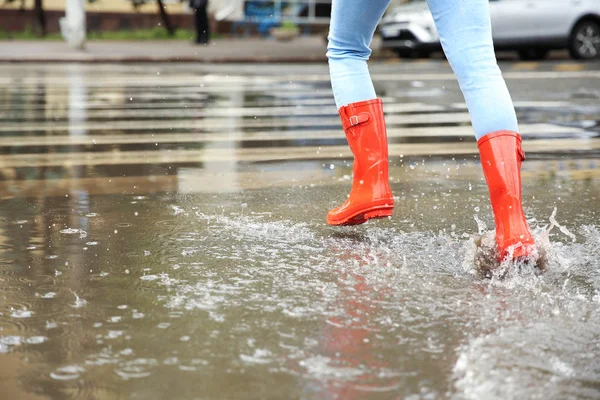 Kobieta z czerwonymi gumowymi butami biegnąca w Puddle, zbliżenie. Deszczowa pogoda — Zdjęcie stockowe