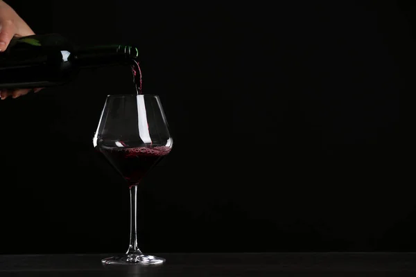 Donna versare il vino in vetro sul tavolo contro sfondo nero, primo piano con spazio per il testo — Foto Stock