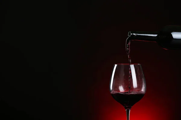 Versare il vino dalla bottiglia in vetro su sfondo scuro, spazio per il testo — Foto Stock