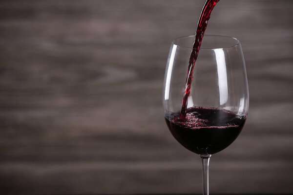 Pouring wine into glass on wooden background, space for text