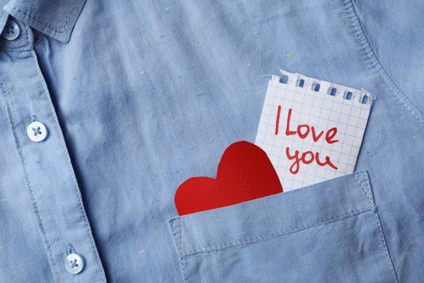 Paper sheet with words I LOVE YOU and heart in pocket of shirt, top view. Space for text