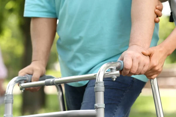 Cuidador ayudando a anciano con el marco de caminar al aire libre, primer plano — Foto de Stock