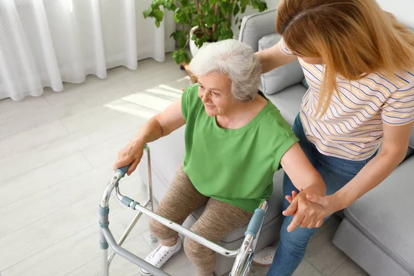 Cuidador ajudando a mulher idosa com quadro de caminhada dentro de casa — Fotografia de Stock
