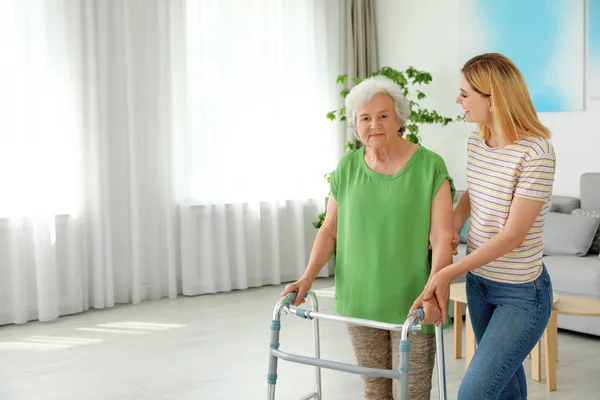 Vaktmästare hjälper äldre kvinna med gång ram inomhus — Stockfoto