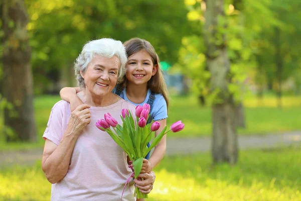 Liten flicka med sin farmor och bukett blommor i parken. Utrymme för text — Stockfoto