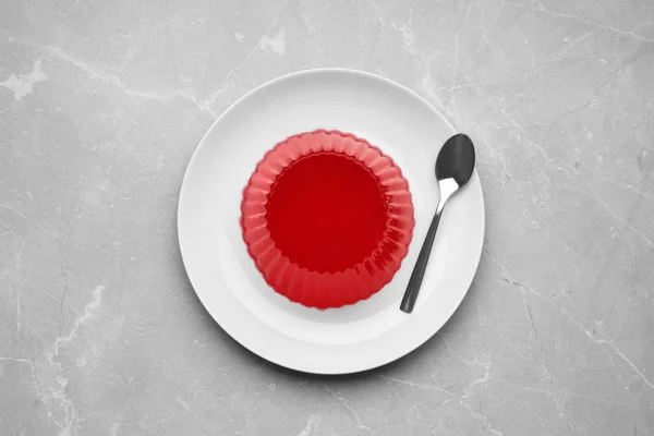 Plate with tasty fruit jelly and spoon on grey table, top view — Stock Photo, Image