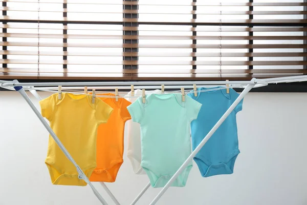 Verschillende schattige baby onesies opknoping op kledinglijn binnenshuis. Wasserij dag — Stockfoto