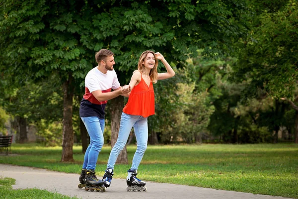 Joven pareja feliz patinaje sobre ruedas en el parque de verano — Foto de Stock