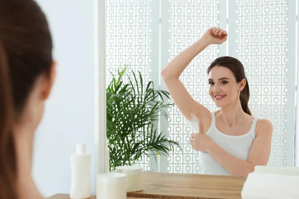 Jeune femme touchant aisselle avec plume près du miroir à la maison. Procédure d'épilation — Photo