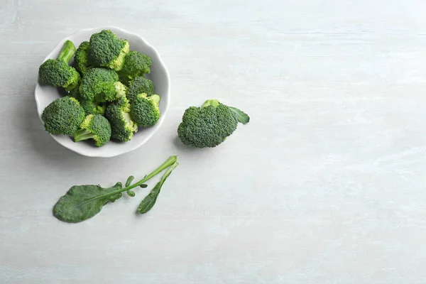 Mangkuk brokoli segar dan daun di meja abu-abu terang, datar berbaring dengan ruang untuk teks — Stok Foto