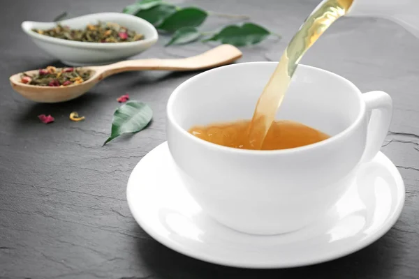 Aromatischer Tee in Tasse auf schwarzem Tisch gießen, Nahaufnahme — Stockfoto