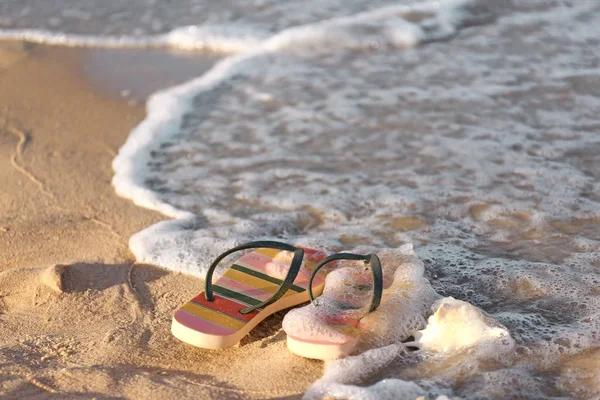 Chanclas con estilo y concha en la arena cerca del mar, espacio para el texto. Accesorios de playa —  Fotos de Stock